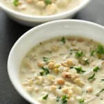 Two bowls of white chicken chili topped with chopped herbs.