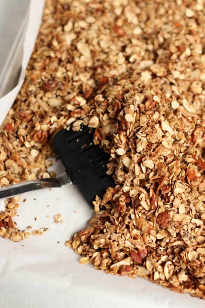 A spatula mixing Power Packed Granola on a baking sheet.