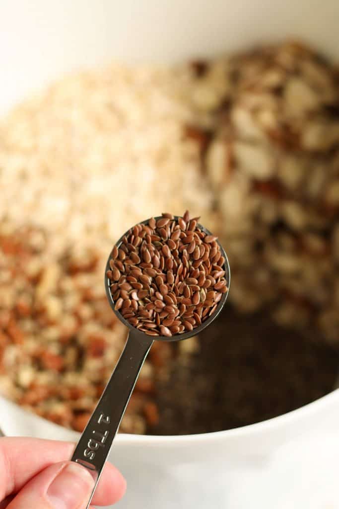 A measuring spoon of flax seeds above a mixing bowl.