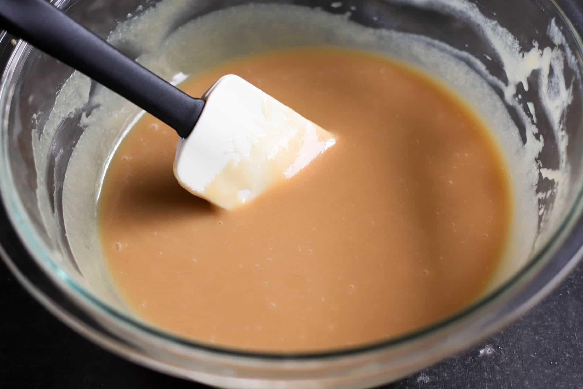 Rubber spatula stirring caramel batter in a glass mixing bowl.