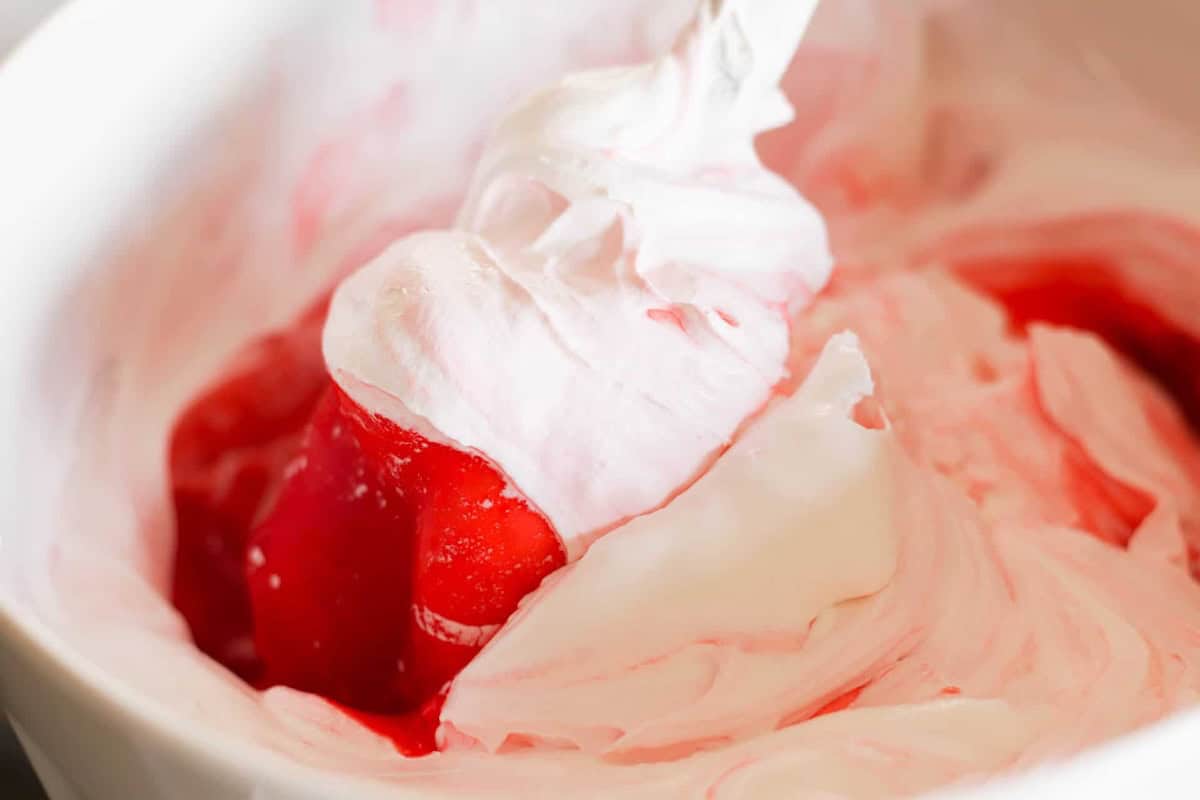 A close-up of whipped cream and strawberry sauce being mixed together in a white bowl.