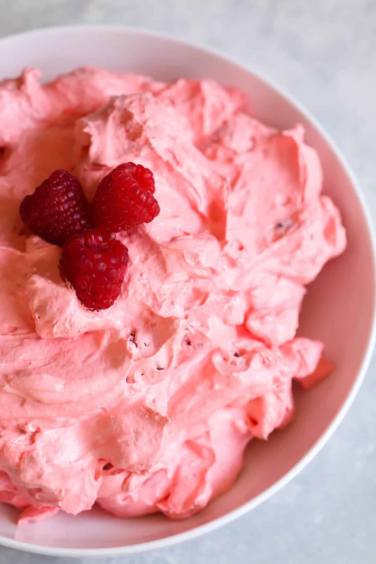 A bowl of pink whipped dessert topped with three fresh raspberries.