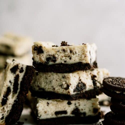 3 Cookies and Cream Cheesecake Bars stacked with one bar leaning against the stack.