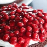 A close-up of a dessert featuring a chocolate cake base topped with a layer of white cream and cherry topping.