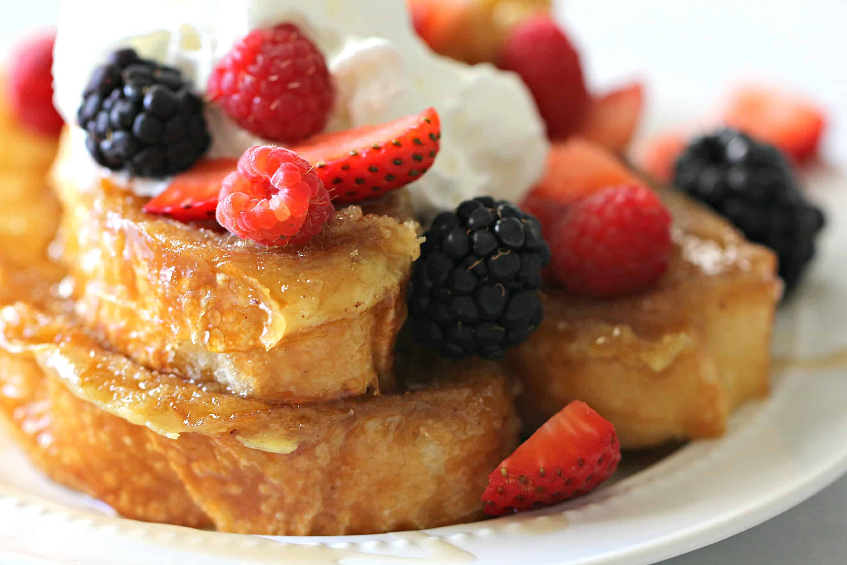 close up of caramelized french toast topped with berries and whipped cream