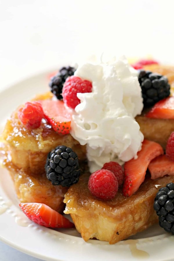 A plate of French toast topped with mixed berries, including raspberries, blackberries, and strawberry slices, finished with a dollop of whipped cream.