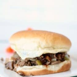 A sandwich with a white bun, filled with ground beef, onions, and pickles, placed on a white surface.