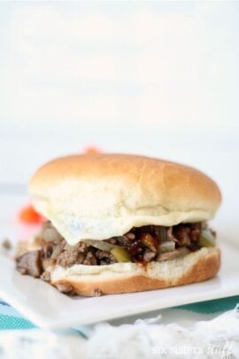 A sandwich with a white bun, filled with ground beef, onions, and pickles, placed on a white surface.