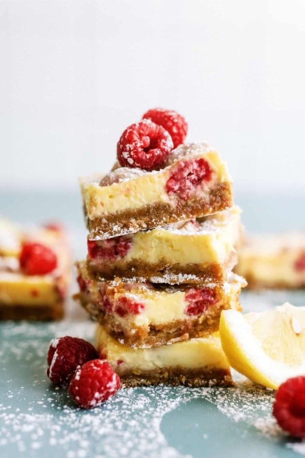 Lemon Raspberry Bars stacked surrounded by fresh raspberries.