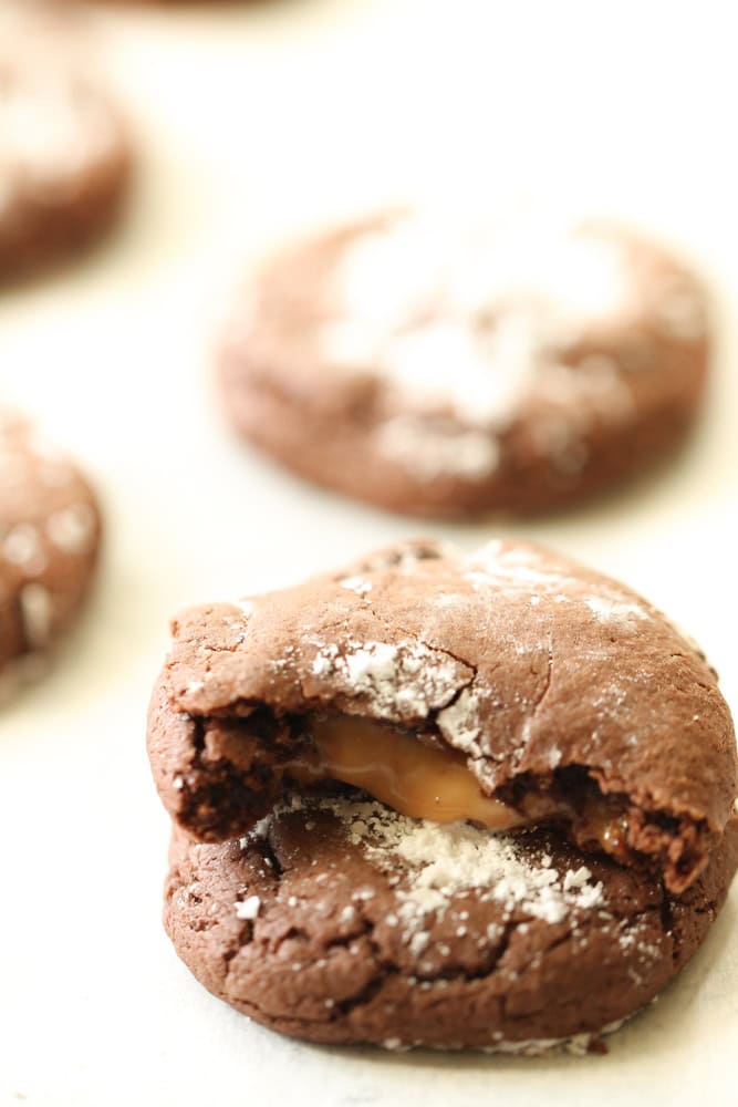 2 stacked rolo cookies topped with powdered sugar with the top one broken in half to show the caramel center.