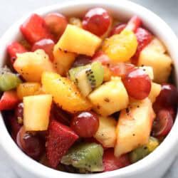 A white bowl filled with a mixed fruit salad containing strawberries, pineapple, grapes, kiwi, and orange segments.