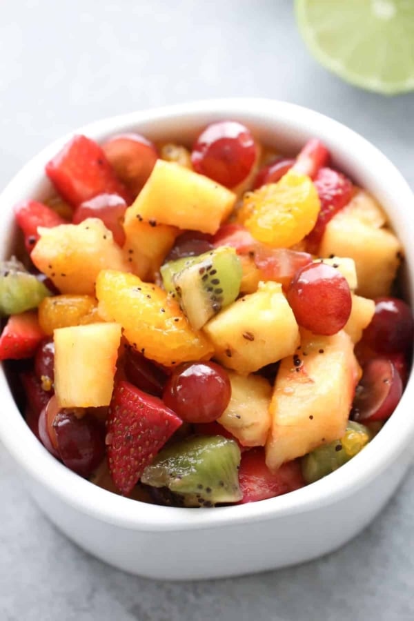 A white bowl filled with a mixed fruit salad containing strawberries, pineapple, grapes, kiwi, and orange segments.