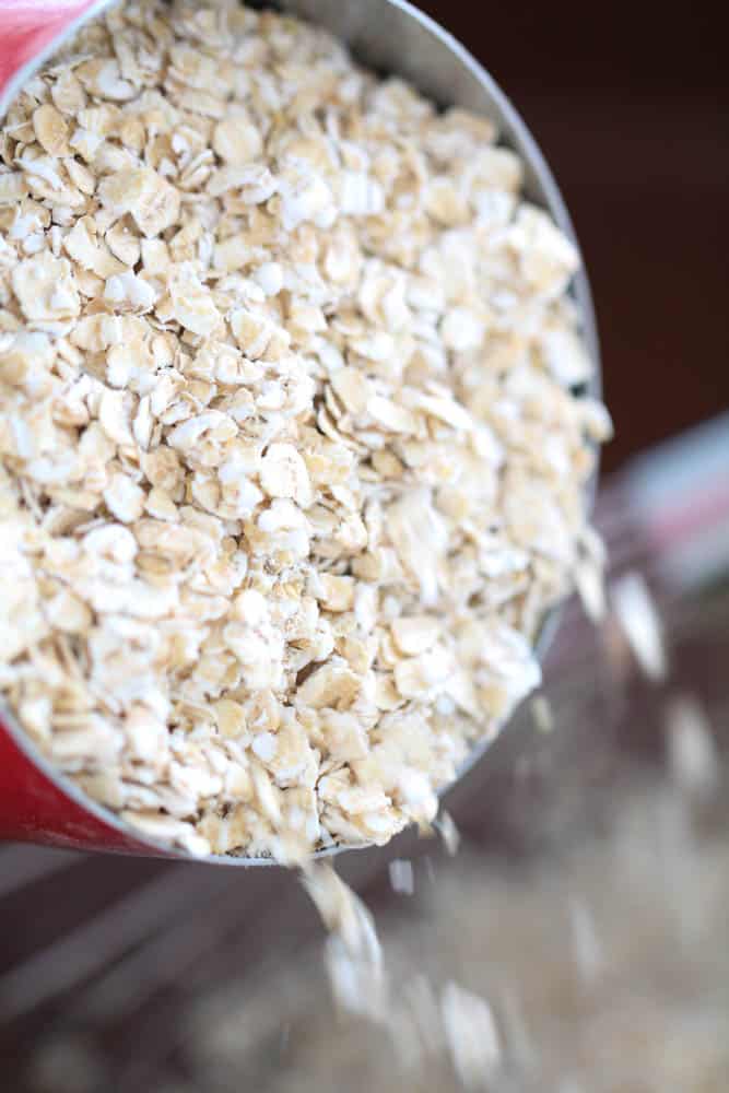 Adding a measuring cup of quick oats to the saucepan.