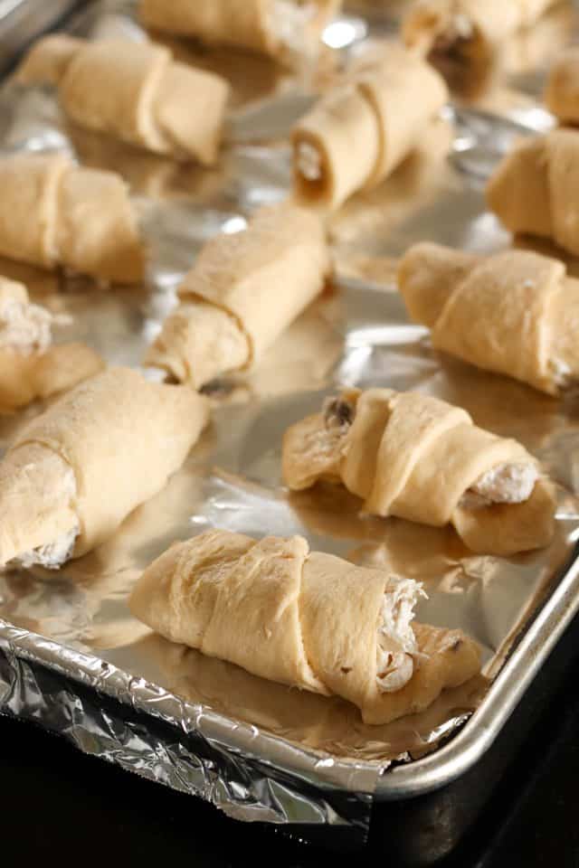 Unbaked crescent rolls filled with a cream mixture placed on a foil-lined baking sheet.