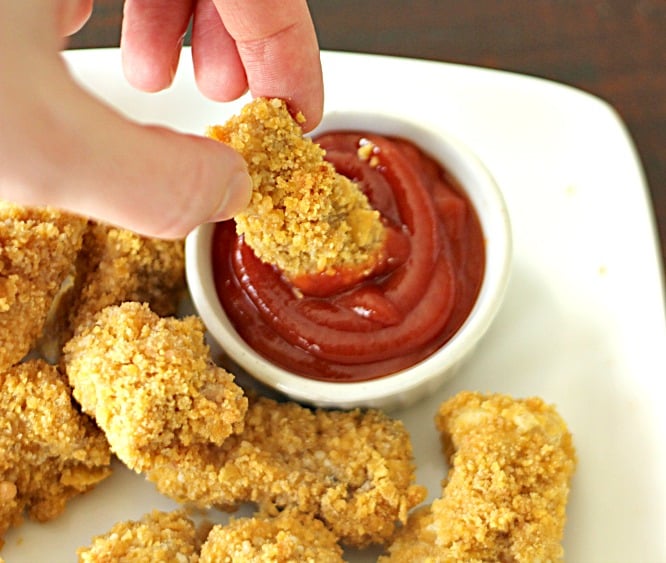 Homemade Baked Chicken Nuggets on a plate, dipping one nugget in ketchup