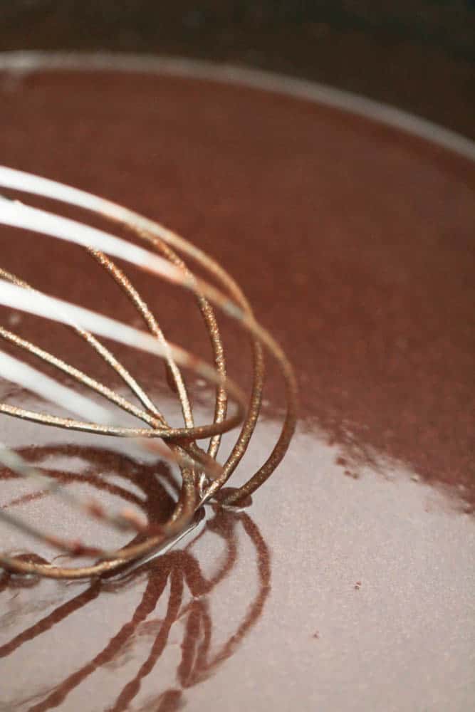 A whisk, whisking chocolate sauce in a saucepan.
