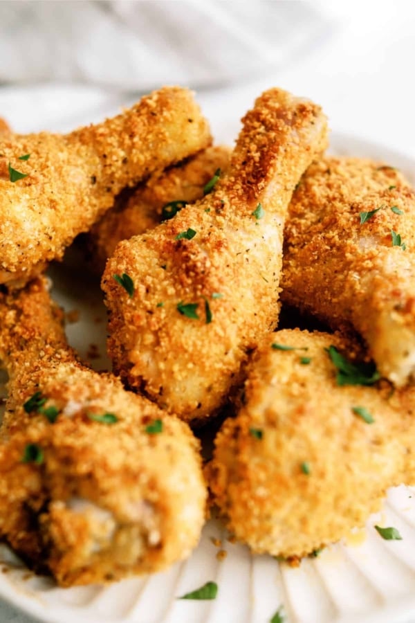 Close-up of several breaded and baked chicken drumsticks garnished with chopped parsley on a white plate.