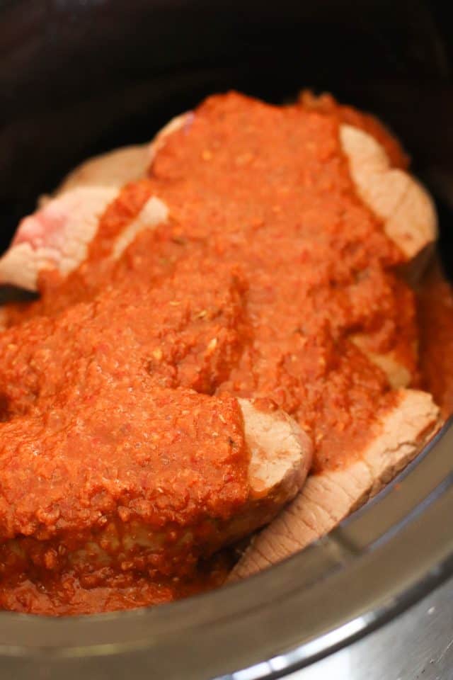 Sliced beef covered in a chunky red tomato sauce in a slow cooker.