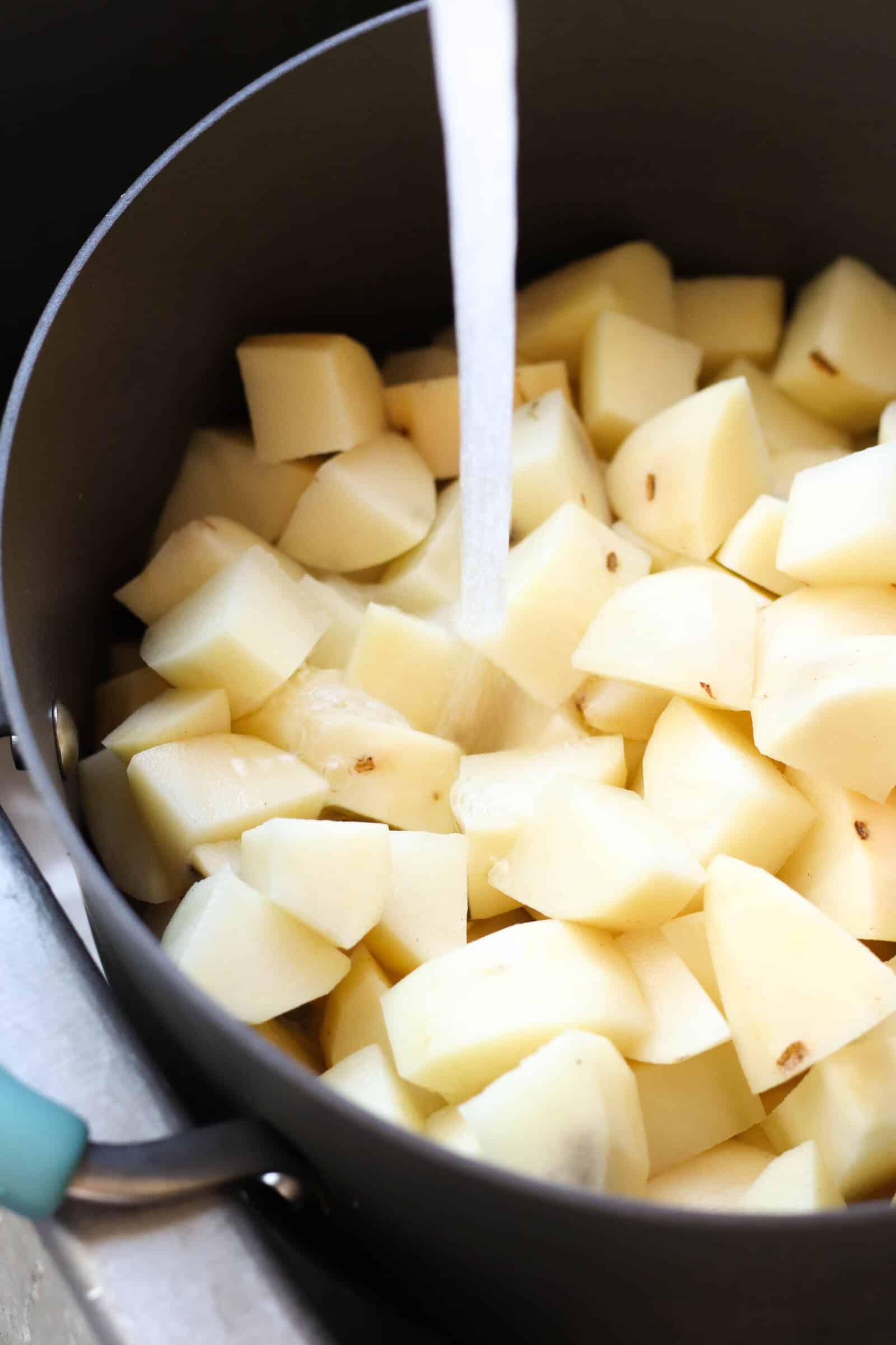 Potatoes in a large pot in the sink, with water pouring into the pot