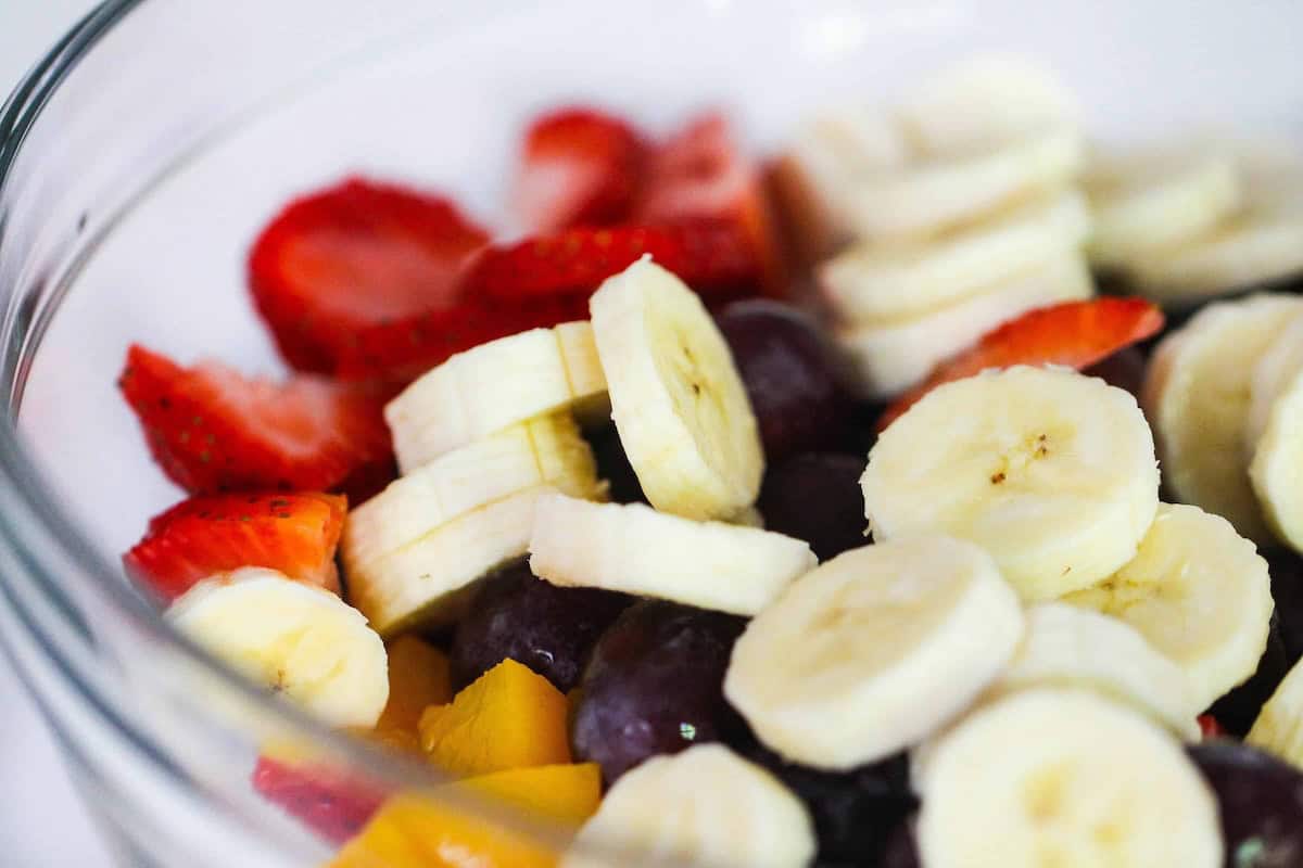 A glass bowl filled with sliced bananas, strawberries, grapes, and mango pieces.