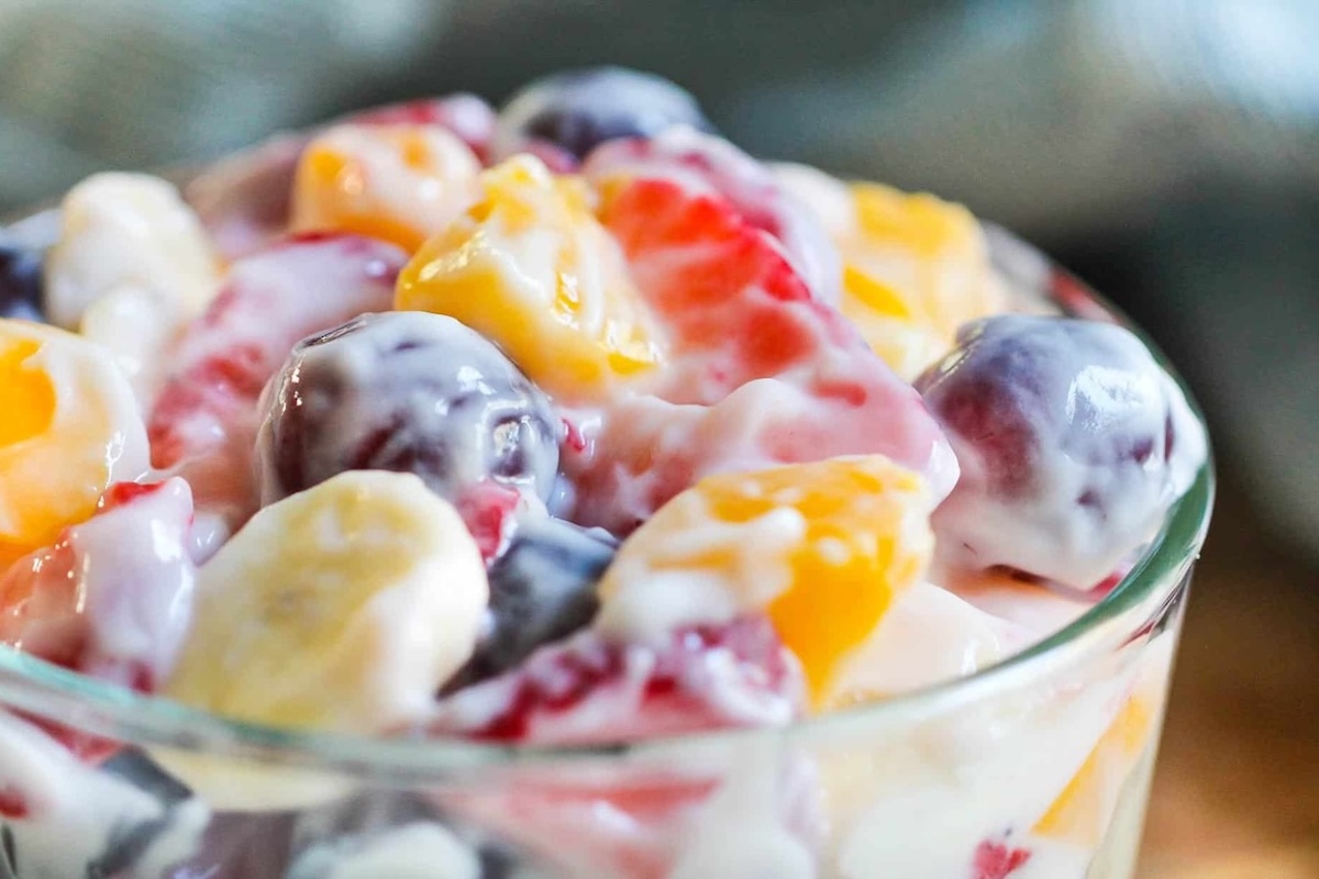 A close-up of a glass bowl filled with mixed fresh fruit pieces coated in creamy yogurt or dressing.