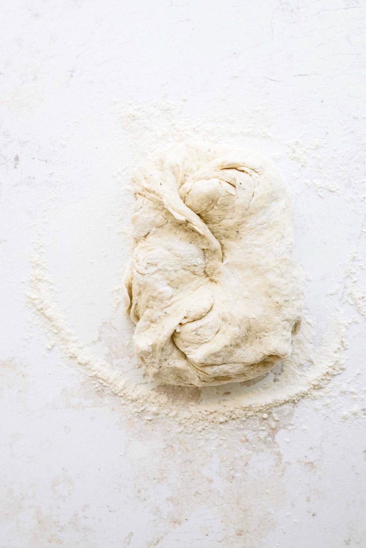 A ball of raw, folded dough rests on a floured white surface.
