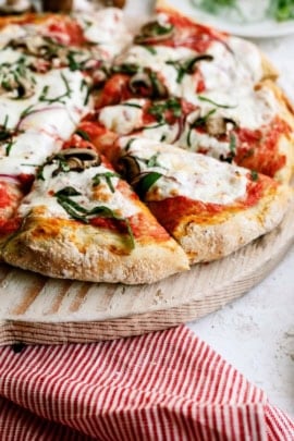 A close-up of a freshly baked pizza topped with melted cheese, tomato sauce, mushrooms, and fresh basil, placed on a wooden pizza board.