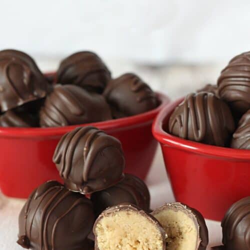 Homemade Reese's Peanut Butter Cup Truffles in two red bowls with some in between the bowls with one cut in half to show the insides.