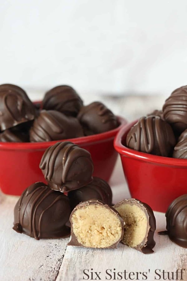 Homemade Reese's Peanut Butter Cup Truffles in two red bowls with some in between the bowls with one cut in half to show the insides.