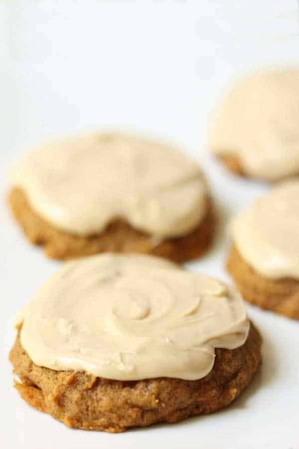 Close-up of four cookies topped with light-colored glaze, placed on a white surface. The cookies have a rough texture and an irregular, rounded shape.