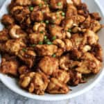 A white bowl filled with chunks of cooked chicken garnished with chopped green onions.
