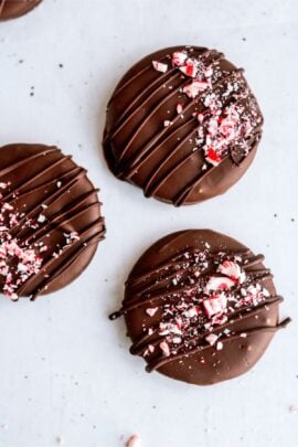 Three chocolate-covered round cookies topped with crushed peppermint candy and drizzled with additional chocolate.