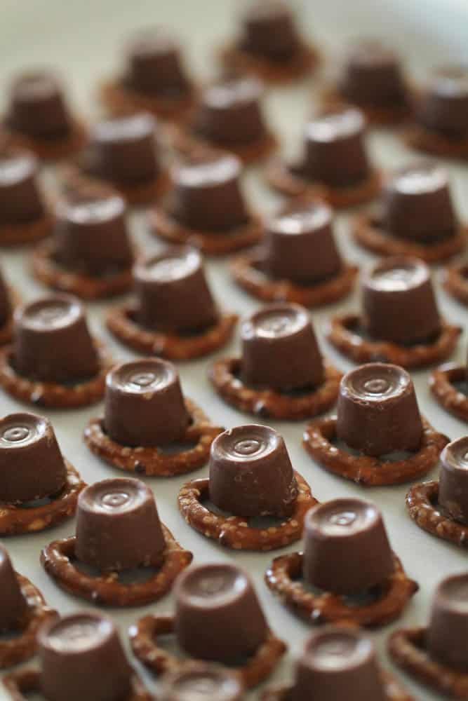 Rolo candies unwrapped sitting on top each pretzel twist on a parchment lined baking sheet.