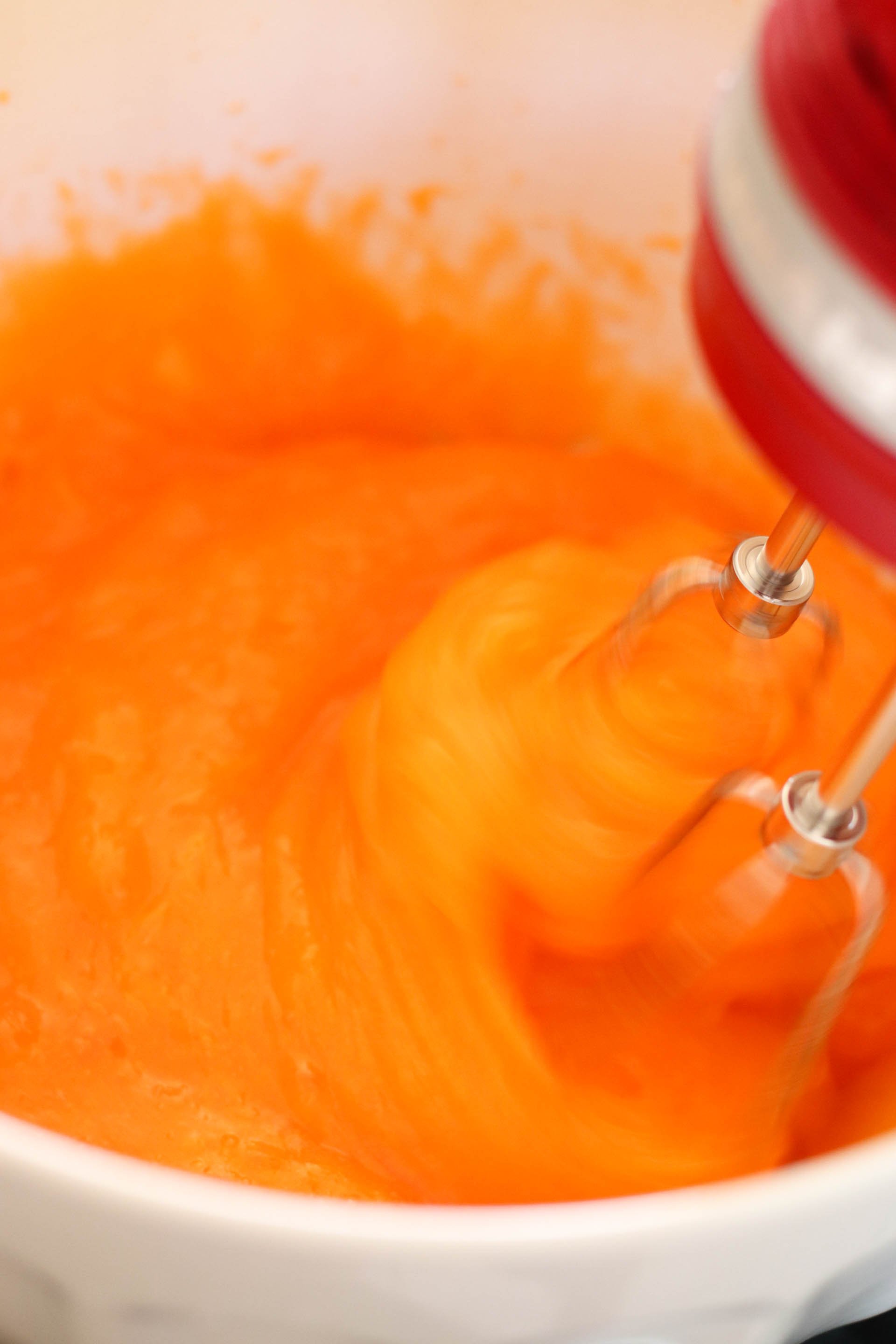 orange jello in a white bowl being mixed with electric mixer