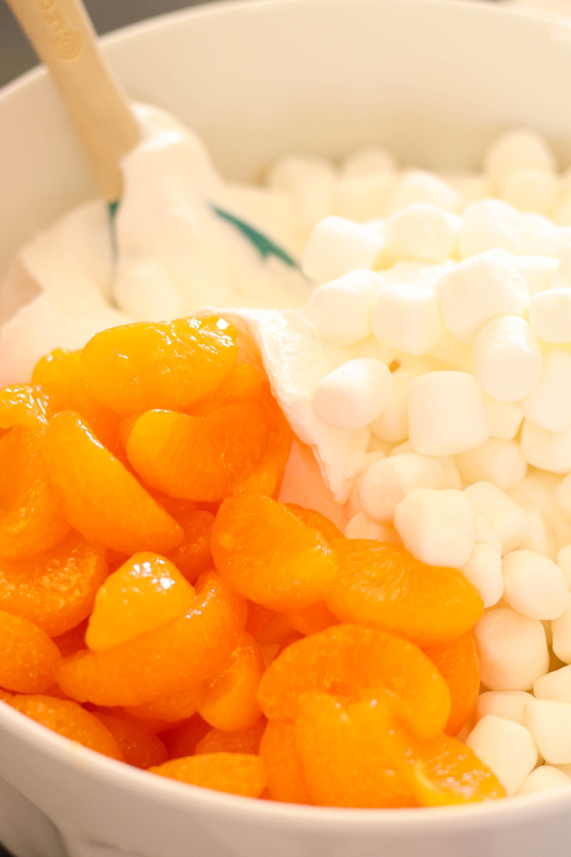cool whip, oranges, and marshmallows being mixed together in a big bowl