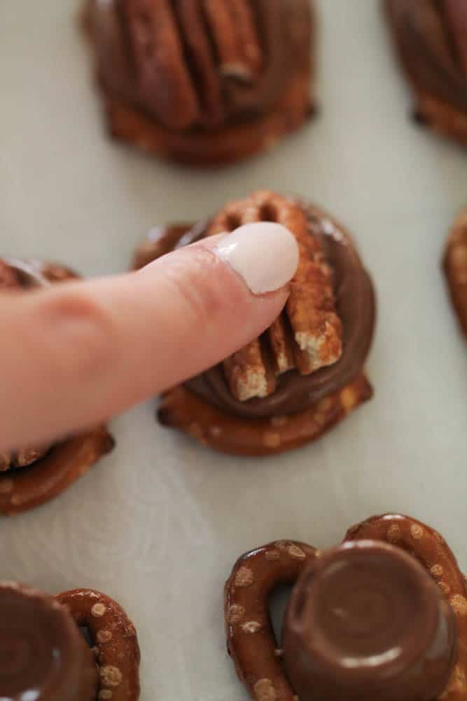 Pressing half a pecan into a melted rolo on top of a pretzel twist.