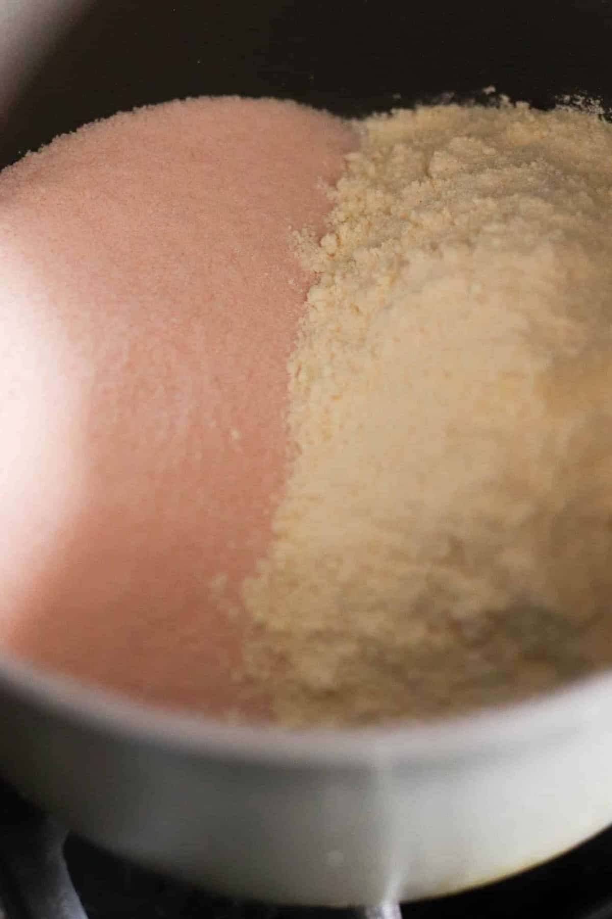 A close-up of a bowl containing pink-colored powder on the left and off-white powder on the right, positioned side by side.