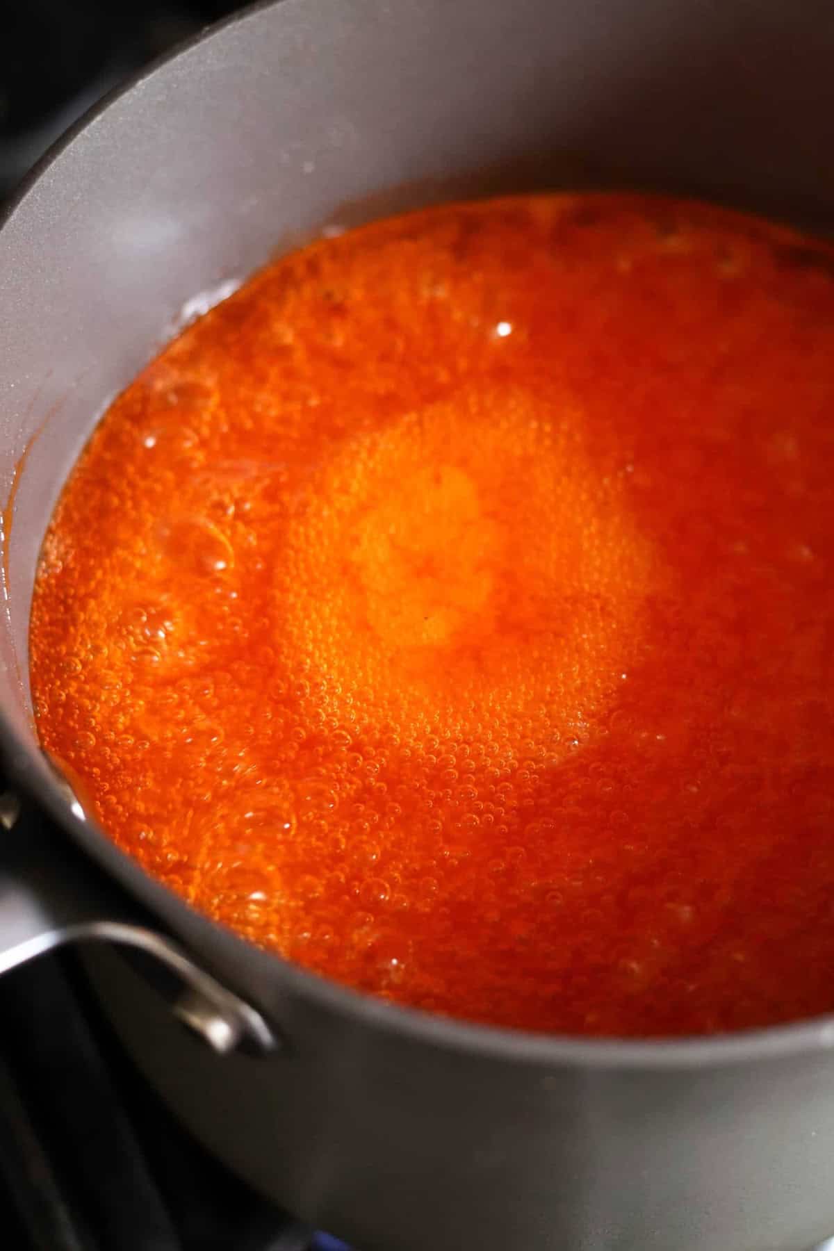 A pot filled with bubbling orange-red liquid simmering on a stove.