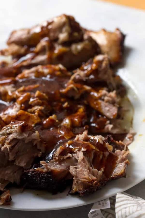Close-up of shredded barbecue pork covered in sauce, served on a white plate.
