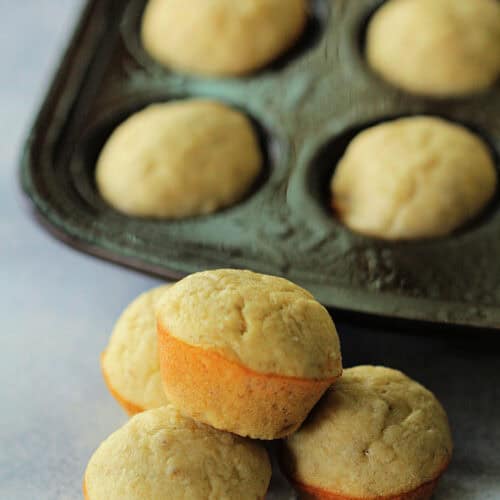 Lion House Banana Bread Muffins stacked on a counter with some muffins in the tin.