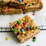 M&M Samoa Blondies cut into squares with one blondie in front surrounded by mini m&m's.