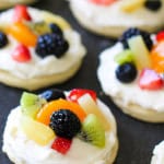 Several Mini Sugar Cookie Fruit Pizzas on a black background.