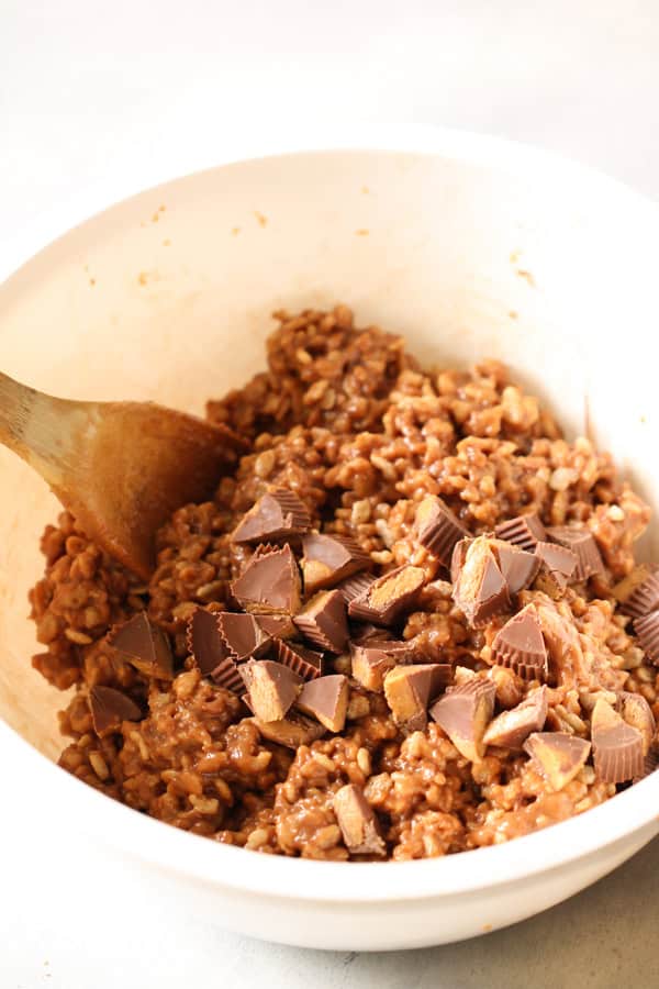 A wooden spoon folding in chopped Reese’s Peanut Butter Cups into the rice krispies mixture.