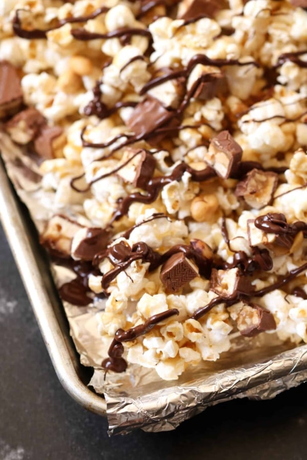 A close-up of a tray of popcorn mixed with chunks of chocolate and drizzled with melted chocolate.