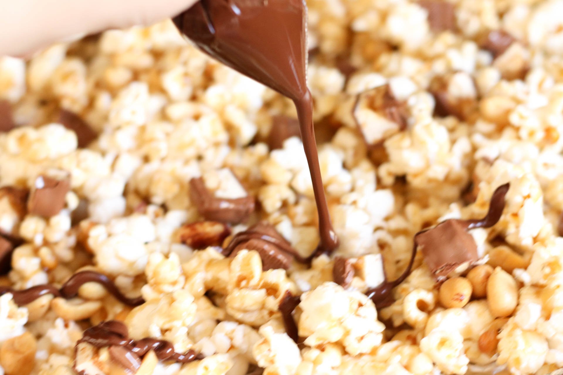 Drizzling chocolate sauce on top of Snickers Popcorn