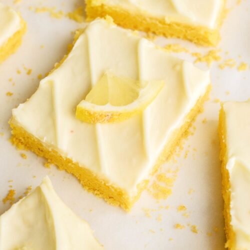 Lemon bars with lemon frosting on a white surface.