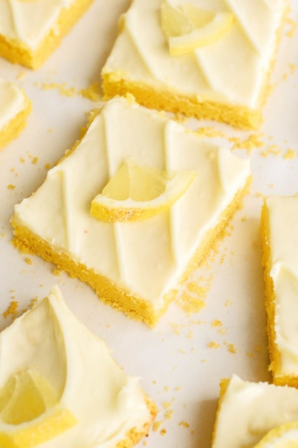 Lemon bars with lemon frosting on a white surface.