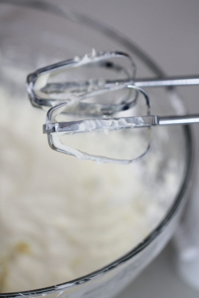 A mixing bowl with a hand mixer hanging over it.