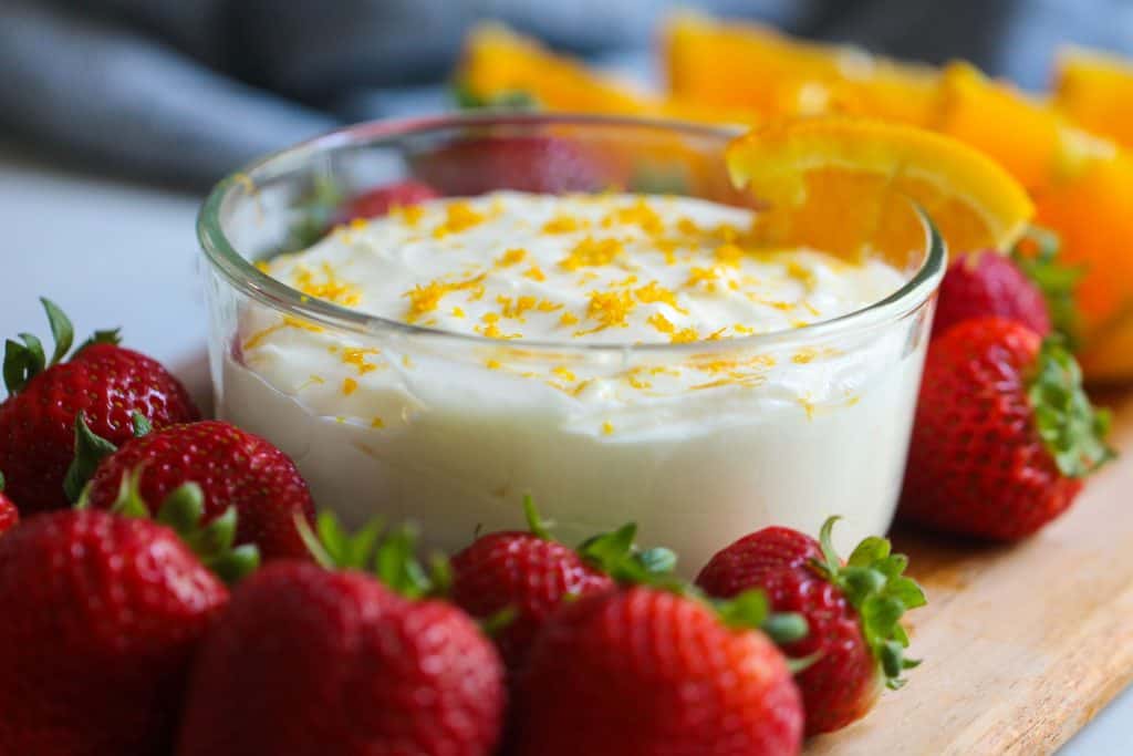 Orange Creamsicle Fruit Dip in a glass bowl surrounded by fresh fruit.