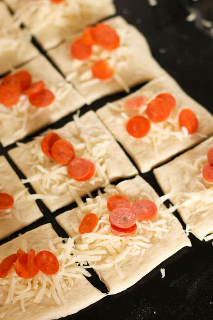 Shredded cheese and mini pepperonis on top of a dough square.